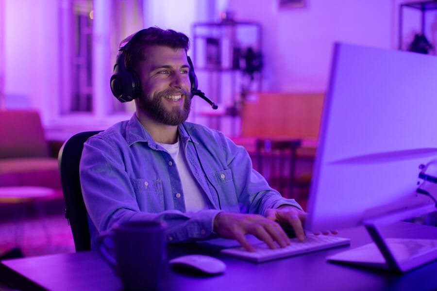 Puntuación seo de mi web conclusión - Hombre sonriente con auriculares trabajando en un ordenador en un ambiente relajado con iluminación en tonos púrpura y azul