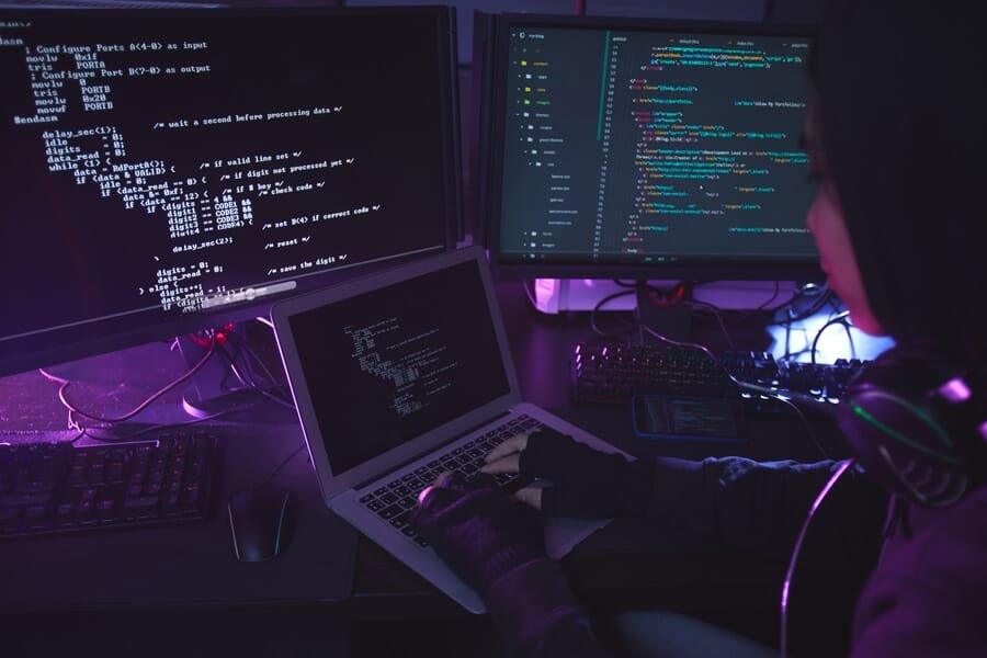 Velocidad de la página web minificación - Persona trabajando frente a múltiples pantallas con código en un entorno oscuro, representando actividades relacionadas con programación o ciberseguridad