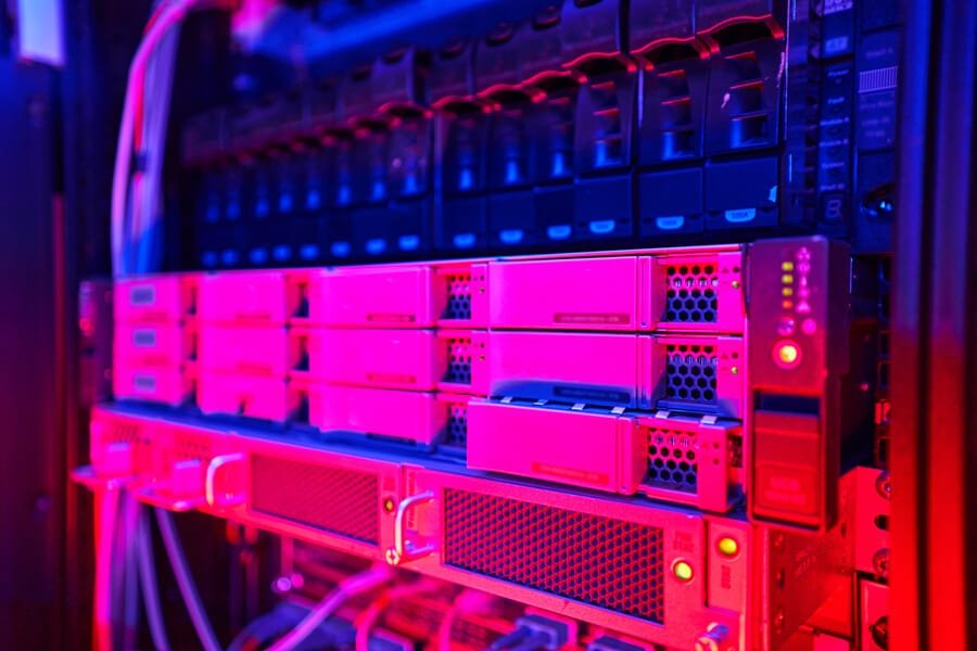 Velocidad de la página web hosting rápido - Servidor de datos en un centro de almacenamiento iluminado con luces rosadas y azules, mostrando equipos de hardware y conexiones tecnológicas